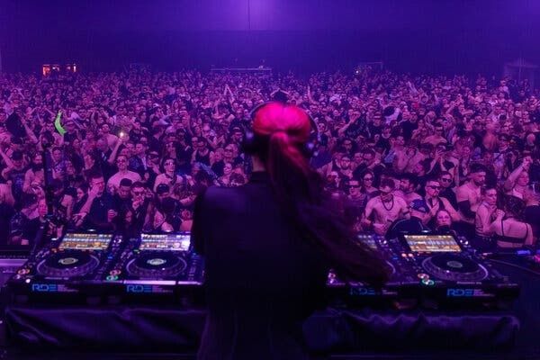 DJ vor dicht gedrängtem Publikum bei einem violett beleuchteten Rave